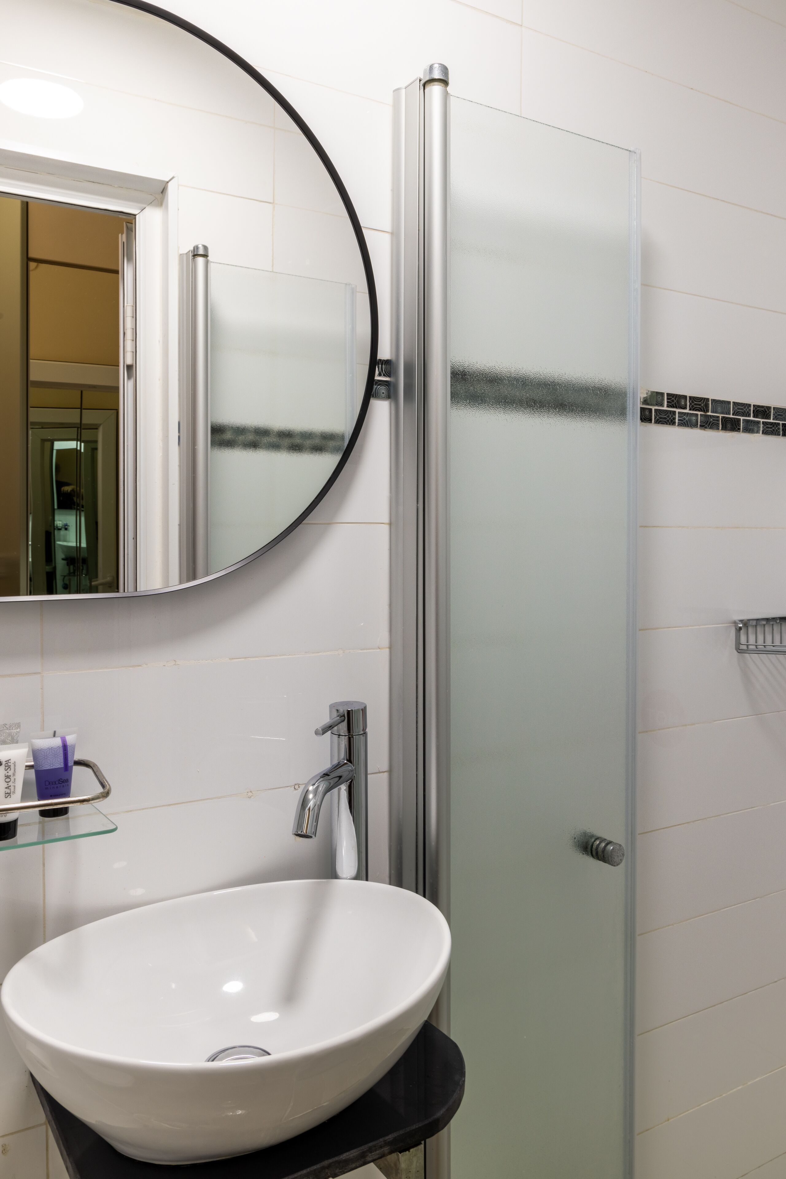Un baño con un lavamanos blanco, un espejo redondo y una ducha con cerramiento de vidrio.