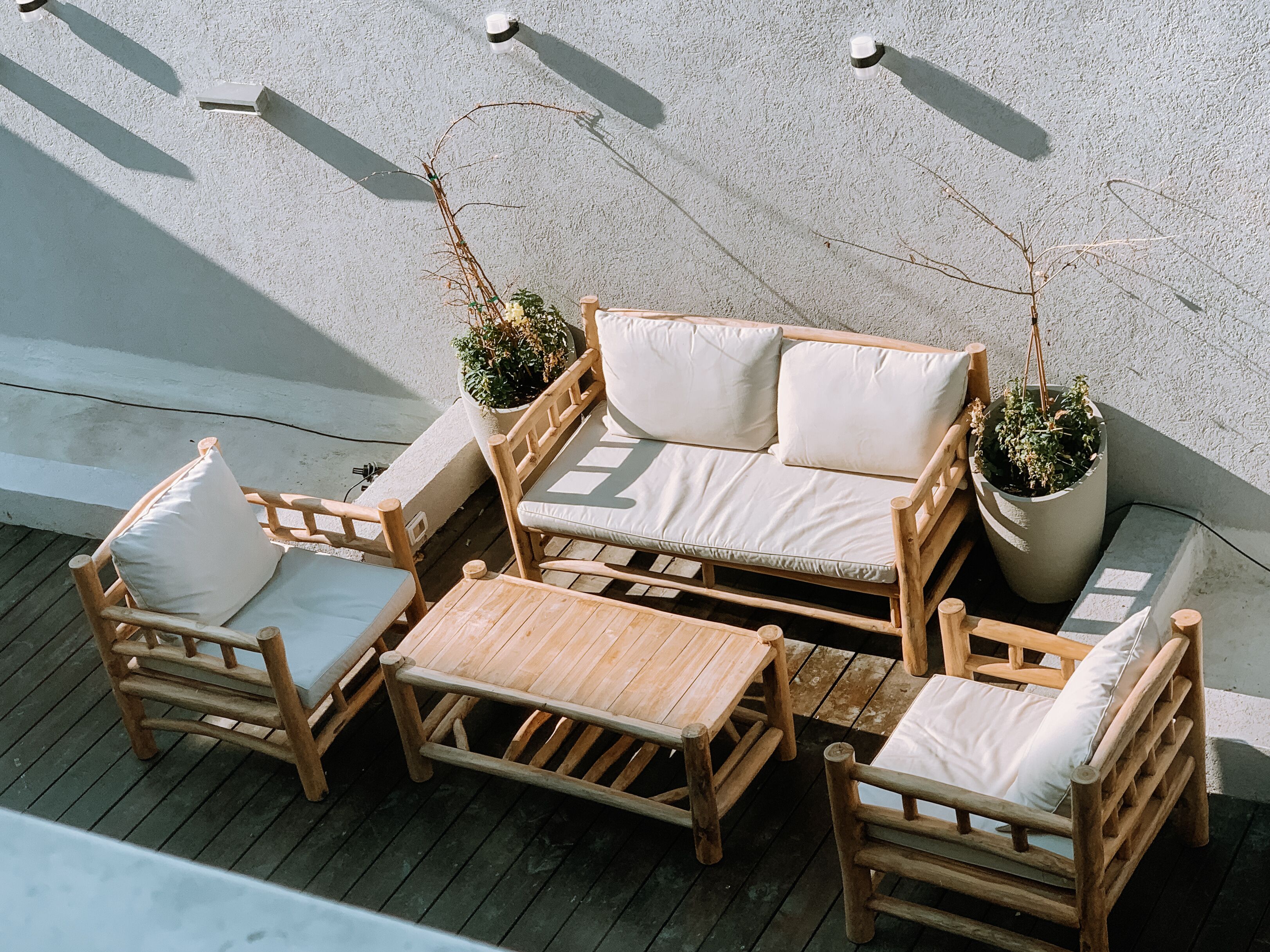 A wooden outdoor seating area with a sofa, two armchairs, and a coffee table, surrounded by potted plants.