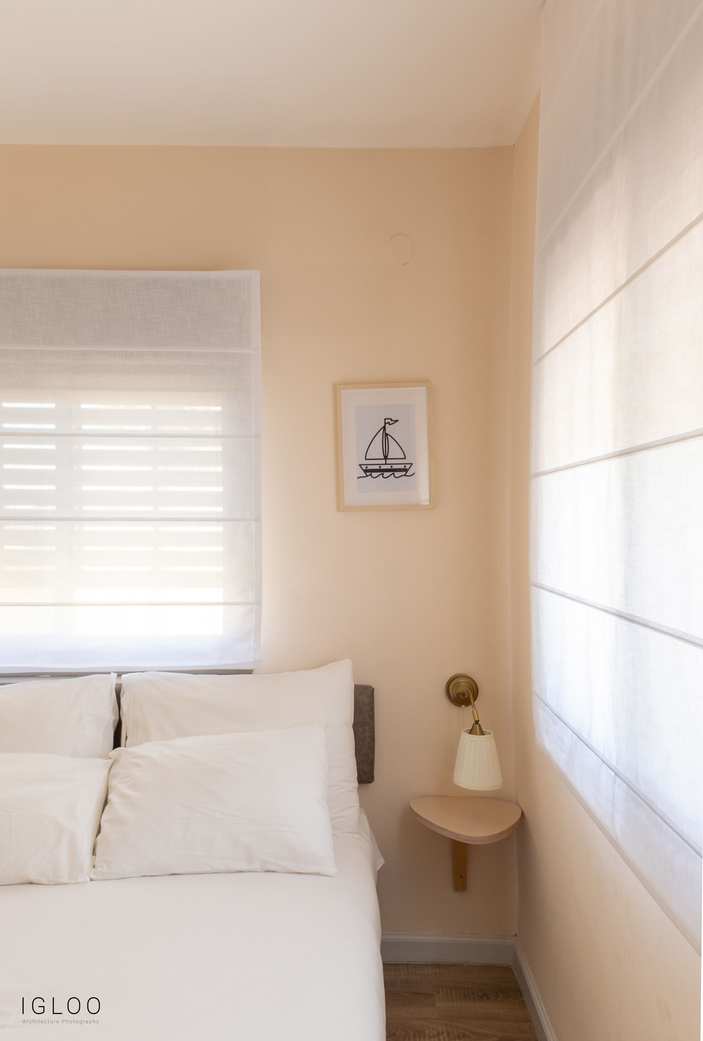 A bedroom with a bed, a bedside table with a lamp, a window with blinds, and a framed picture on the wall.