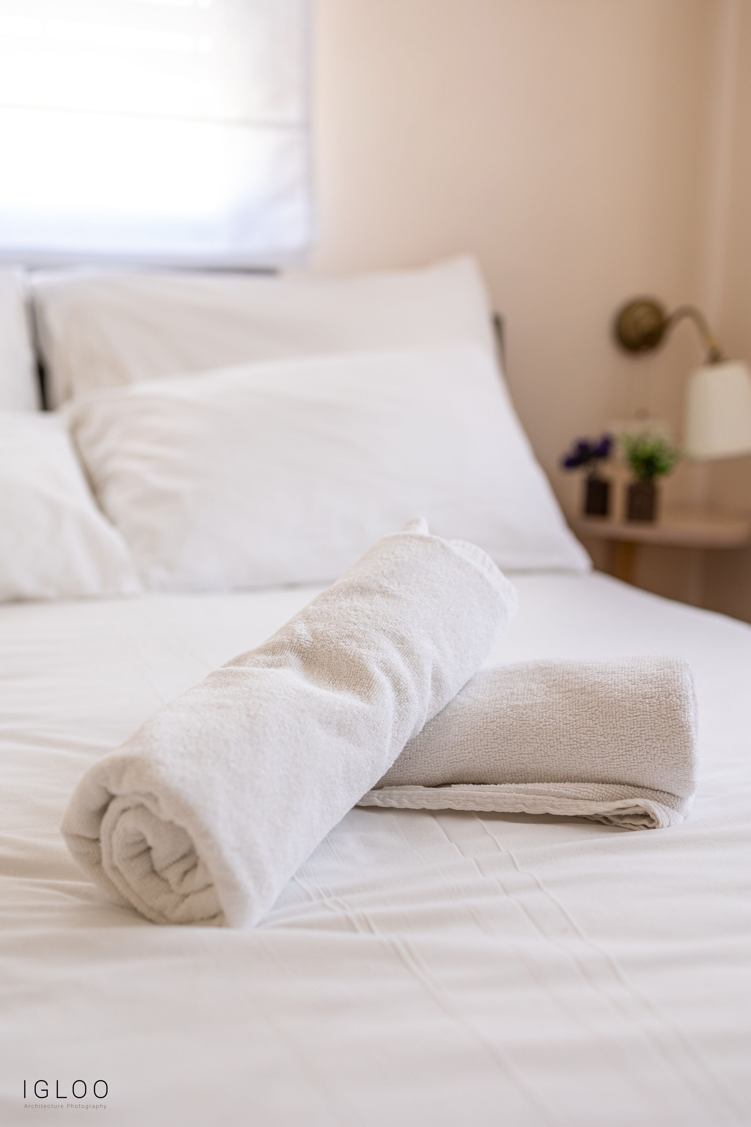 A neatly made bed with white linens and a rolled towel on top.