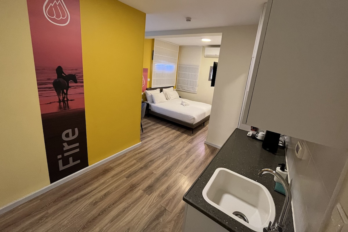 A hotel room with a bed, a bedside table, a sink, and a mirror.