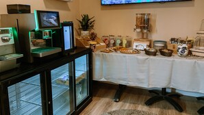 A buffet setup with a variety of food items, a coffee machine, and a television displaying a blue abstract image. - Domus Bat Galim Hotel (Haifa)