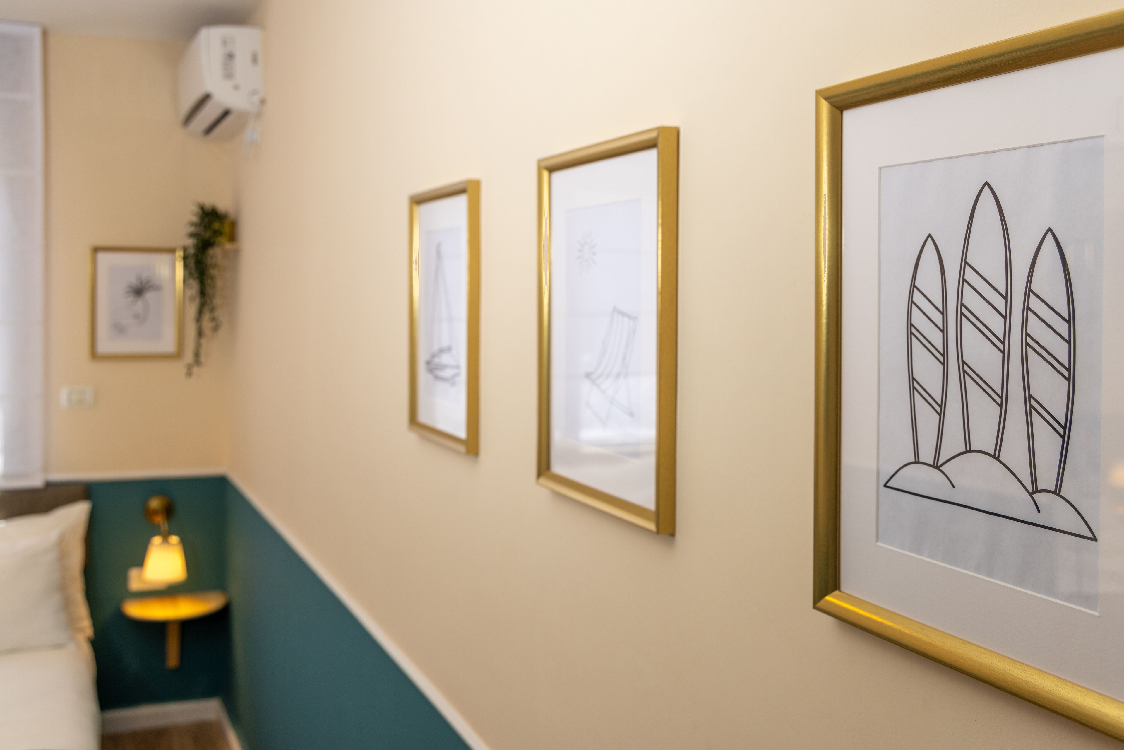 Un couloir avec des œuvres d’art encadrées accrochées aux murs, une lampe et un lit à l’arrière-plan.
