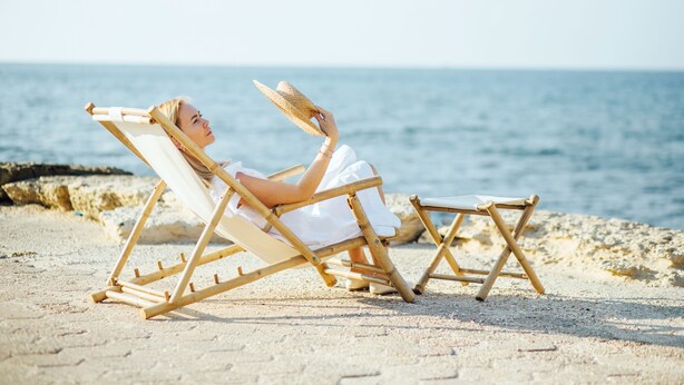 A person reclining on a beach chair, holding a straw hat, with the ocean in the background. - Domus Bat Galim Hotel (Haifa)