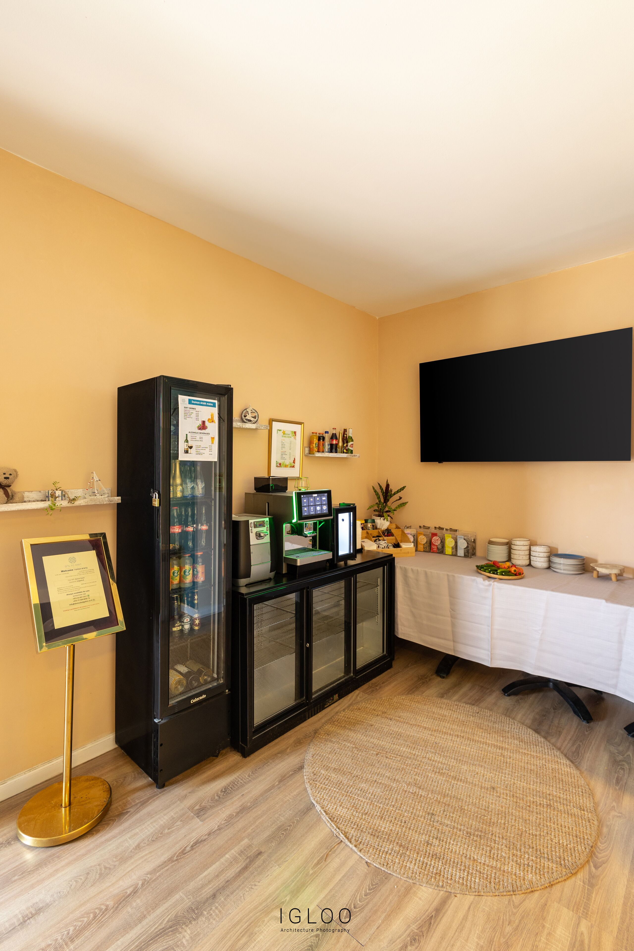 A room with a black refrigerator, a flat-screen TV, a buffet table with plates and drinks, and a framed certificate on the wall.
