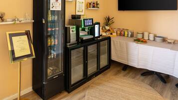 A room with a black refrigerator, a flat-screen TV, a buffet table with plates and drinks, and a framed certificate on the wall.
