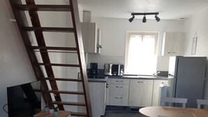 Eine kleine Küche mit weißen Schränken, einem Holztisch und einem Fernseher auf einem Holzboden.