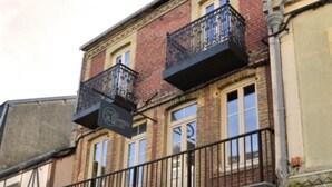 Ein Gebäude mit Ziegelverkleidung, mehreren Fenstern und einem Balkon mit Metallgeländer.