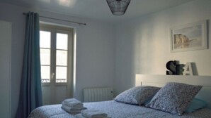 Ein Schlafzimmer mit einem Bett, einem Heizkörper, einem Fenster mit Vorhängen und einer Wandleuchte.