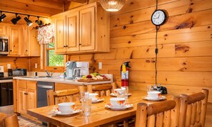 A wooden cabin interior with a kitchen, dining area, and a clock on the wall. - 3 BR/2.5 BA NEAR PARKWAY, GAME ROOM, FIREPLACE, HOT TUB,REAL LOG CABIN,PETS OK! (Pigeon Forge)