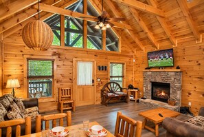 A log cabin interior with a fireplace, wooden furniture, and a television mounted on the wall. - 3 BR/2.5 BA NEAR PARKWAY, GAME ROOM, FIREPLACE, HOT TUB,REAL LOG CABIN,PETS OK! (Pigeon Forge)