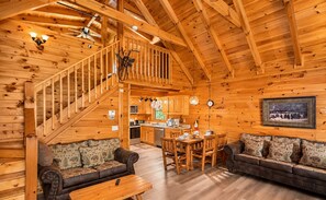 A wooden cabin interior with a dining area, kitchen, and a staircase leading to an upper level. - 3 BR/2.5 BA NEAR PARKWAY, GAME ROOM, FIREPLACE, HOT TUB,REAL LOG CABIN,PETS OK! (Pigeon Forge)