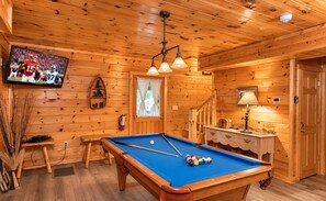 A wooden interior with a pool table, a television mounted on the wall, and a staircase. - 3 BR/2.5 BA NEAR PARKWAY, GAME ROOM, FIREPLACE, HOT TUB,REAL LOG CABIN,PETS OK! (Pigeon Forge)
