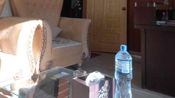 Una sala de estar con un sofá, una mesa de centro de vidrio, una botella de agua y un televisor en la pared.
