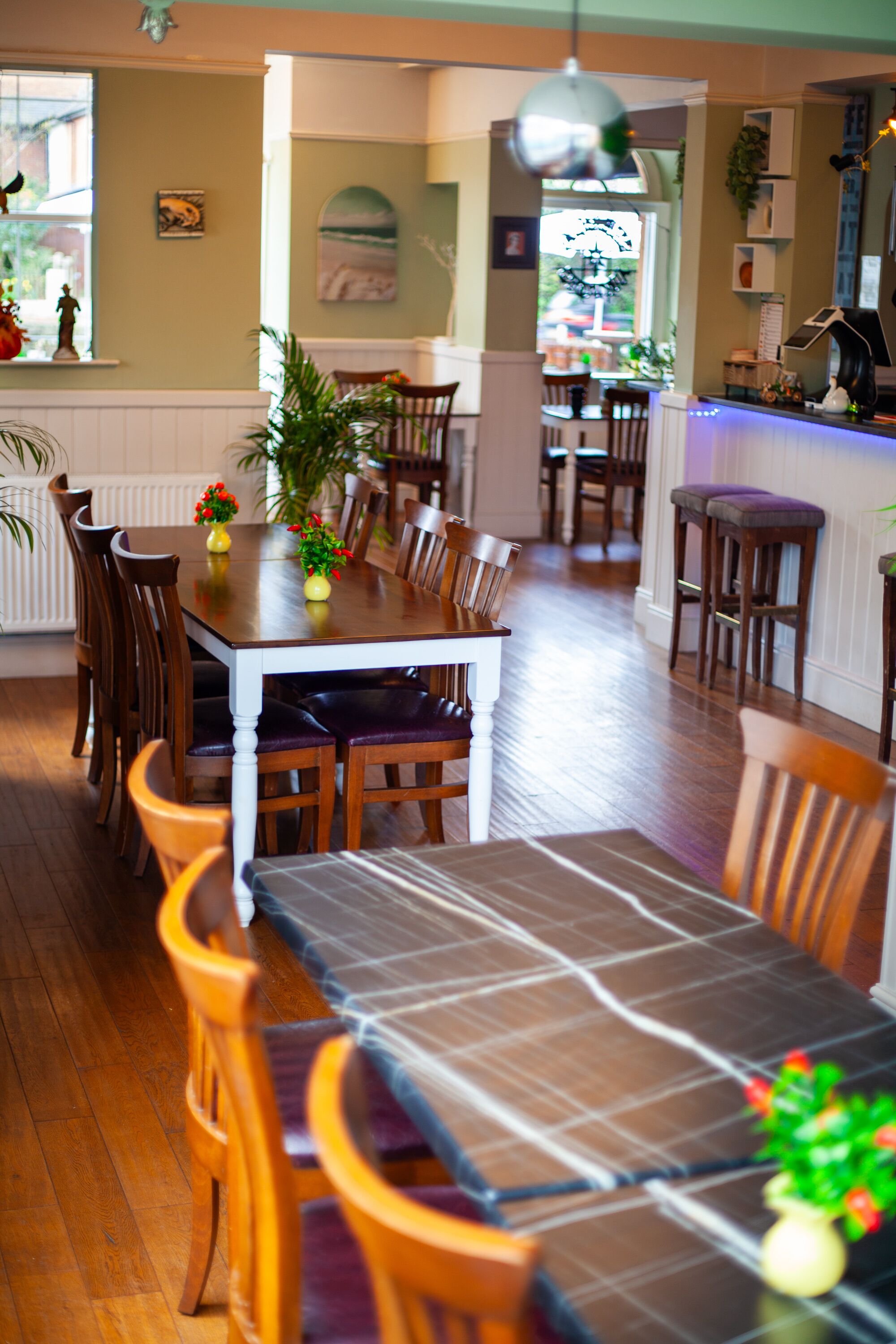 A dining area with wooden tables and chairs, a kitchen in the background, and a view of the street.