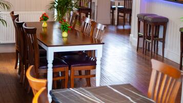A dining area with wooden tables and chairs, a kitchen in the background, and a view of the street.