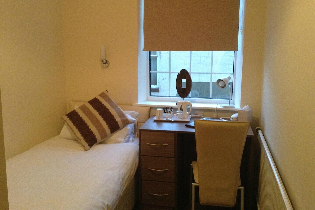 Une petite pièce comprenant un lit, un bureau, une chaise, une fenêtre donnant sur un paysage agréable et un miroir fixé au mur.