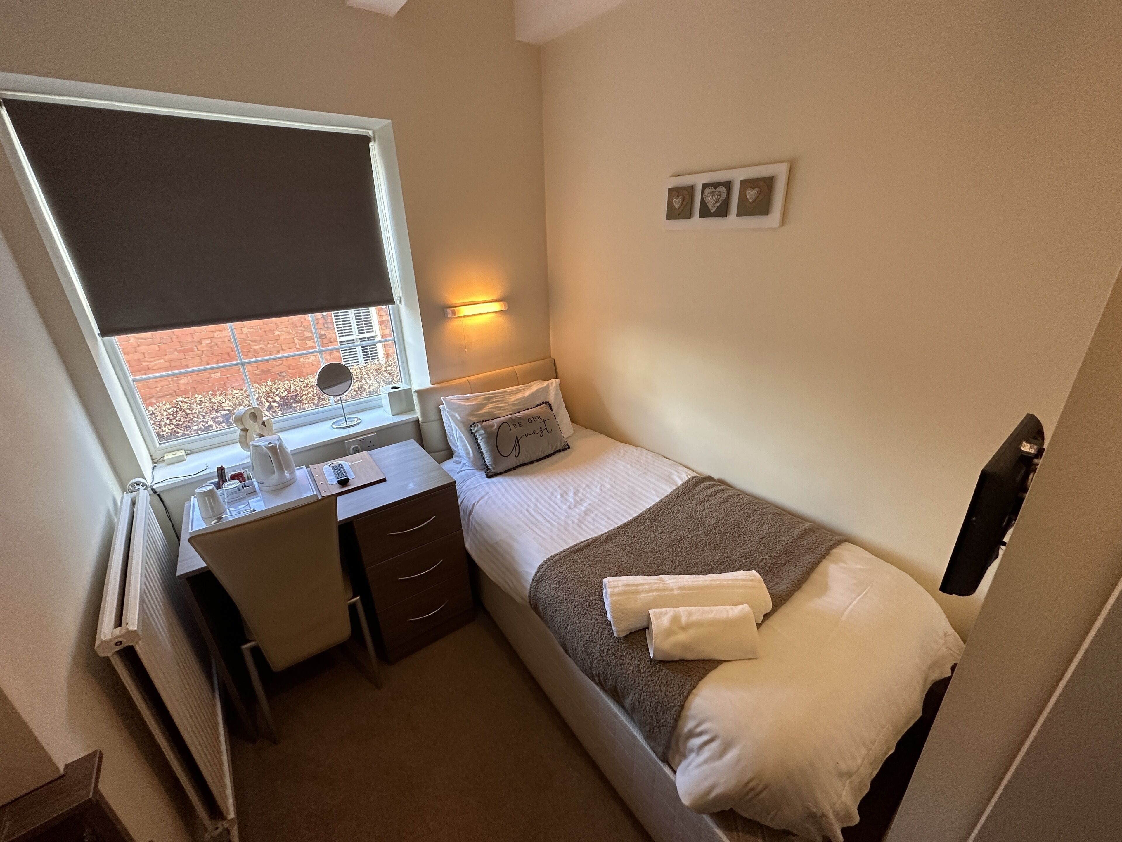 Un dormitorio con cama, mesita de noche, escritorio y ventana.