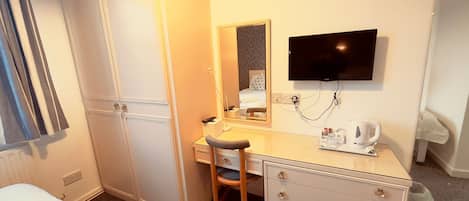 Habitación de hotel con cama, escritorio con silla, televisión, espejo y hervidor de agua.