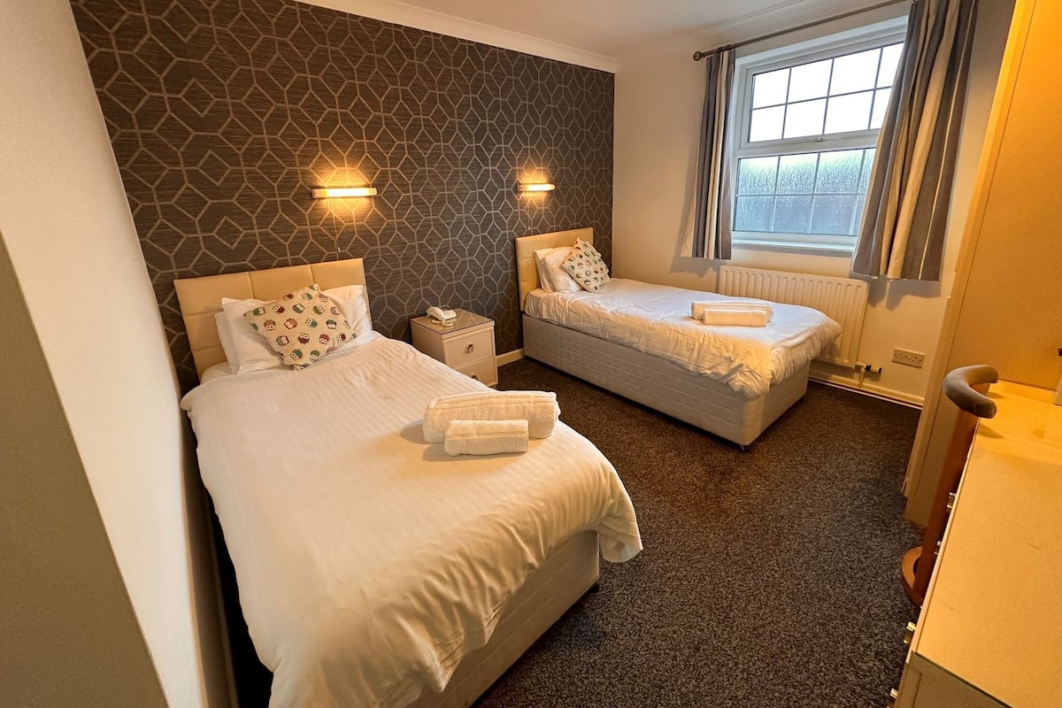 Une chambre d’hôtel avec deux lits, un mur à motifs, une fenêtre avec des rideaux et un radiateur.