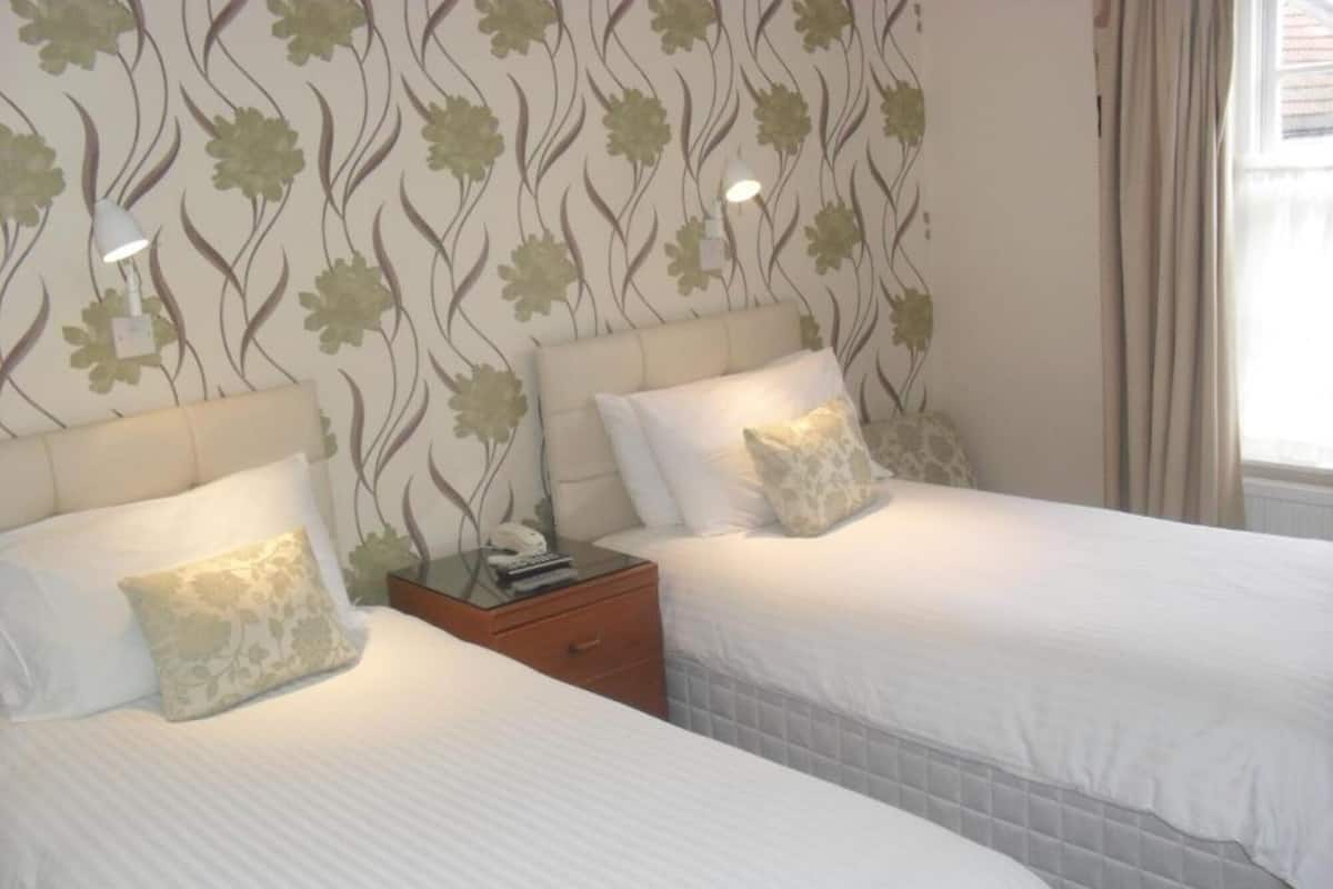 Une chambre d’hôtel avec deux lits, une table de chevet et une fenêtre avec des rideaux.