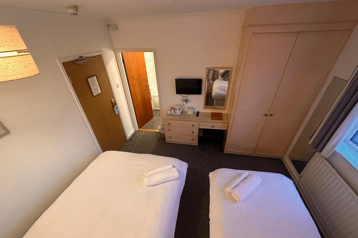 Une chambre d’hôtel avec deux lits, un bureau, un miroir et une télévision.