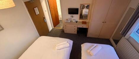 A hotel room with two beds, a desk, a mirror, and a television.