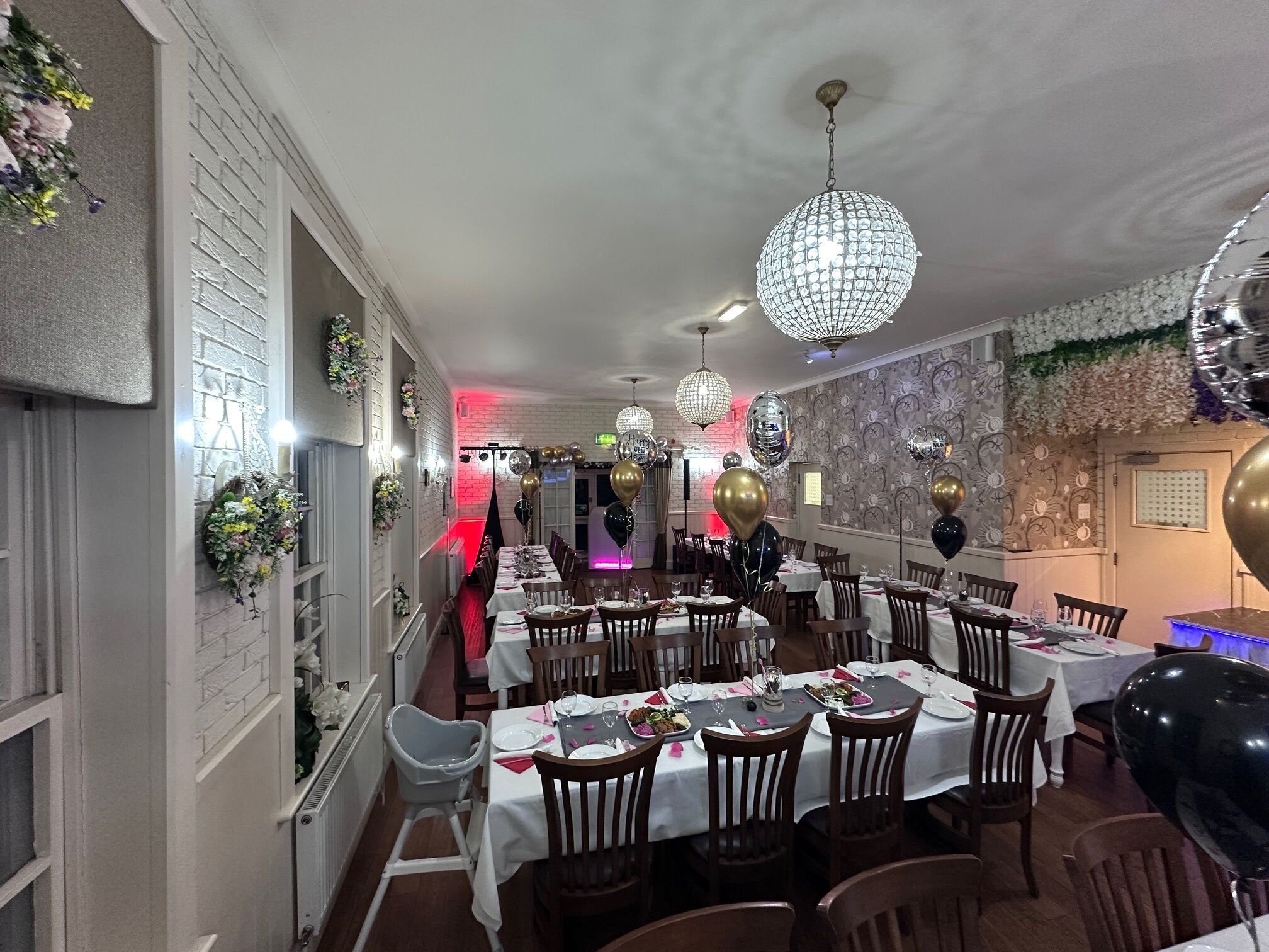 Un restaurant avec de nombreuses tables dressées pour le service, un lustre et des ballons décoratifs.
