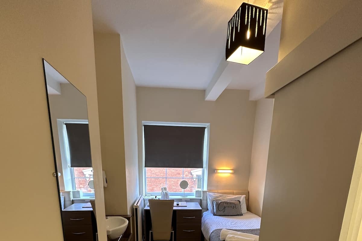 Une chambre d’hôtel de taille réduite, comprenant un lit, un bureau, une chaise et un grand miroir.