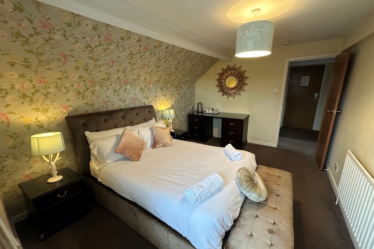Une chambre à coucher comprenant un lit, des tables de chevet, une commode, un miroir et une porte.