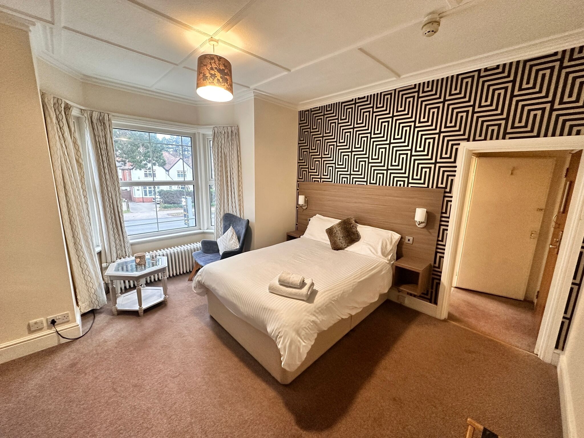 A hotel room with a large bed, a chair, a small table, a radiator, and a window with curtains.