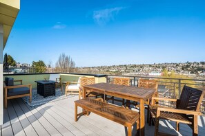 Une terrasse en bois, aménagée avec du mobilier d’extérieur, notamment une table et des chaises, offrant une vue sur le paysage urbain.