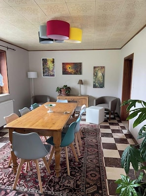 Ein Essbereich mit einem Holztisch, blau-grauen Stühlen, einem gemusterten Teppich und einer Decke mit floralen Kacheln.