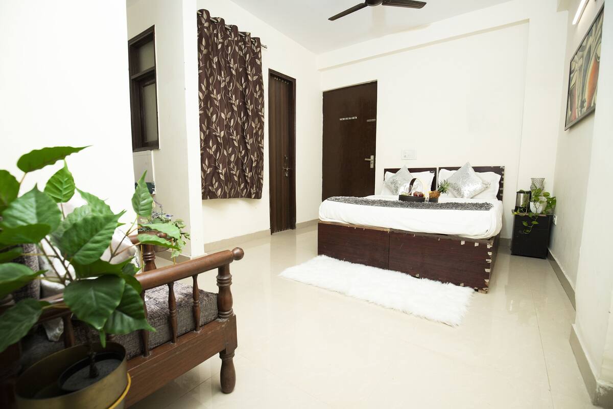 A bedroom with a bed, a wooden bench, a white rug, a ceiling fan, and a potted plant.