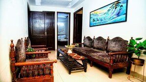 A traditional living room with wooden furniture, a sofa, a bench, and a painting on the wall. - Hotel Royal Avenue By F9 Hotels (New Delhi)