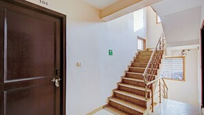 A staircase with a metal railing leading to a higher floor, a door labeled 103 and 104, and a green exit sign on the wall. - Hotel Royal Avenue By F9 Hotels (New Delhi)