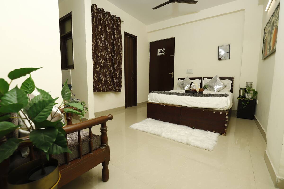 A bedroom with a bed, a wooden bench, a white furry rug, and a potted plant.
