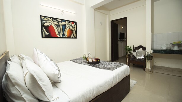 A modern bedroom with a bed, pillows, a painting, and a small table with a fruit bowl. - Hotel Royal Avenue By F9 Hotels (New Delhi)