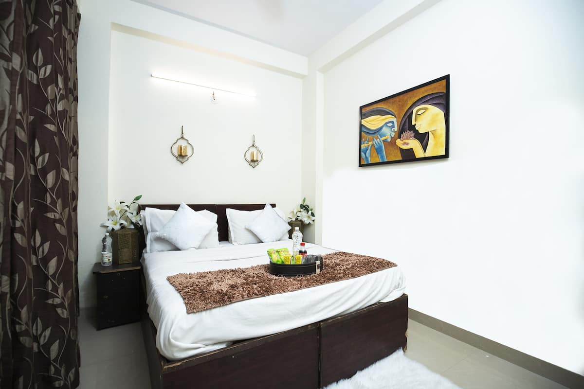 A bedroom with a bed, bedside tables, a nightstand, a wall-mounted artwork, and a window with curtains.