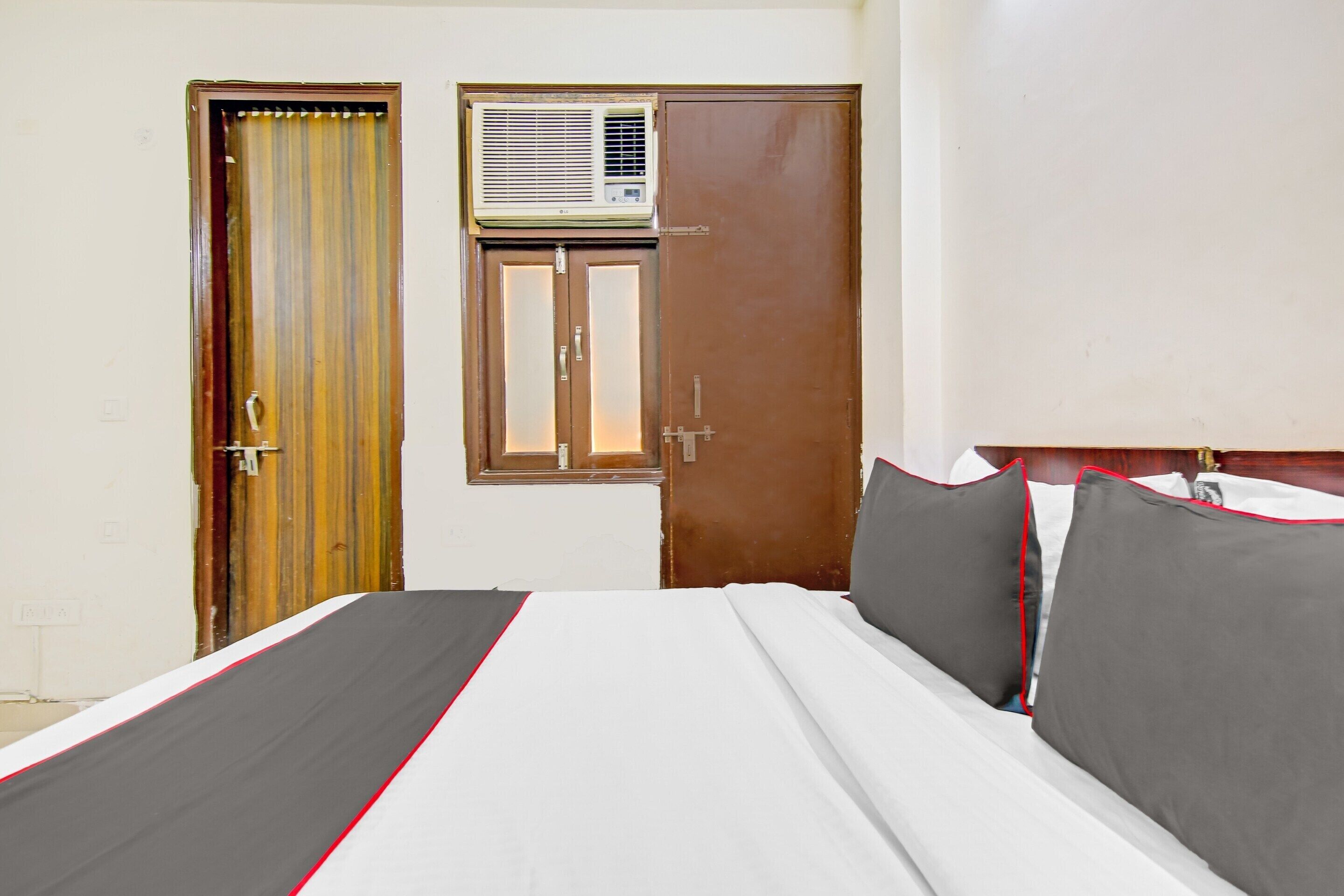 A hotel room with a bed, a window with an air conditioner, and a door.