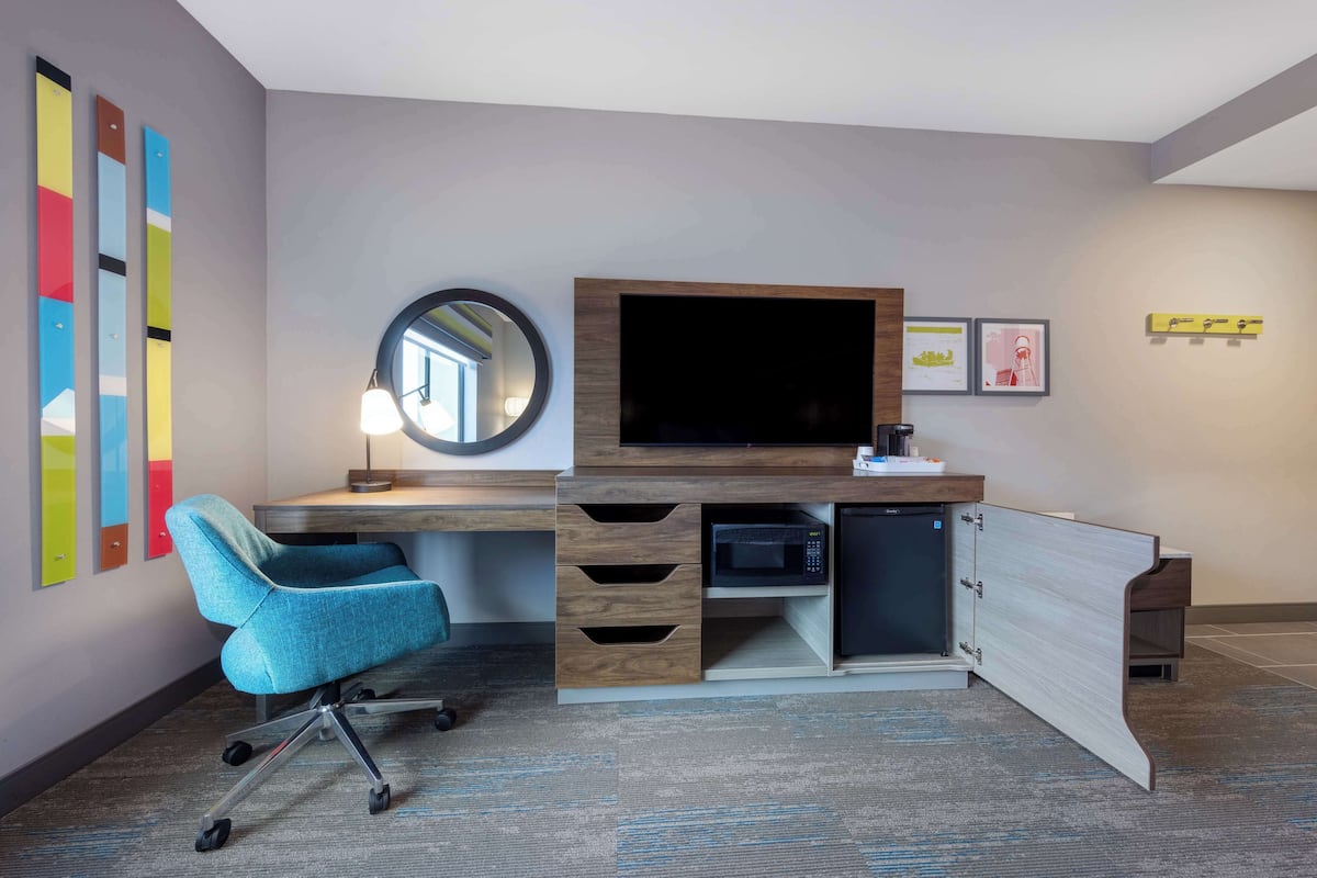 A modern hotel room with a built-in desk, a flat-screen TV, a microwave, and a chair.