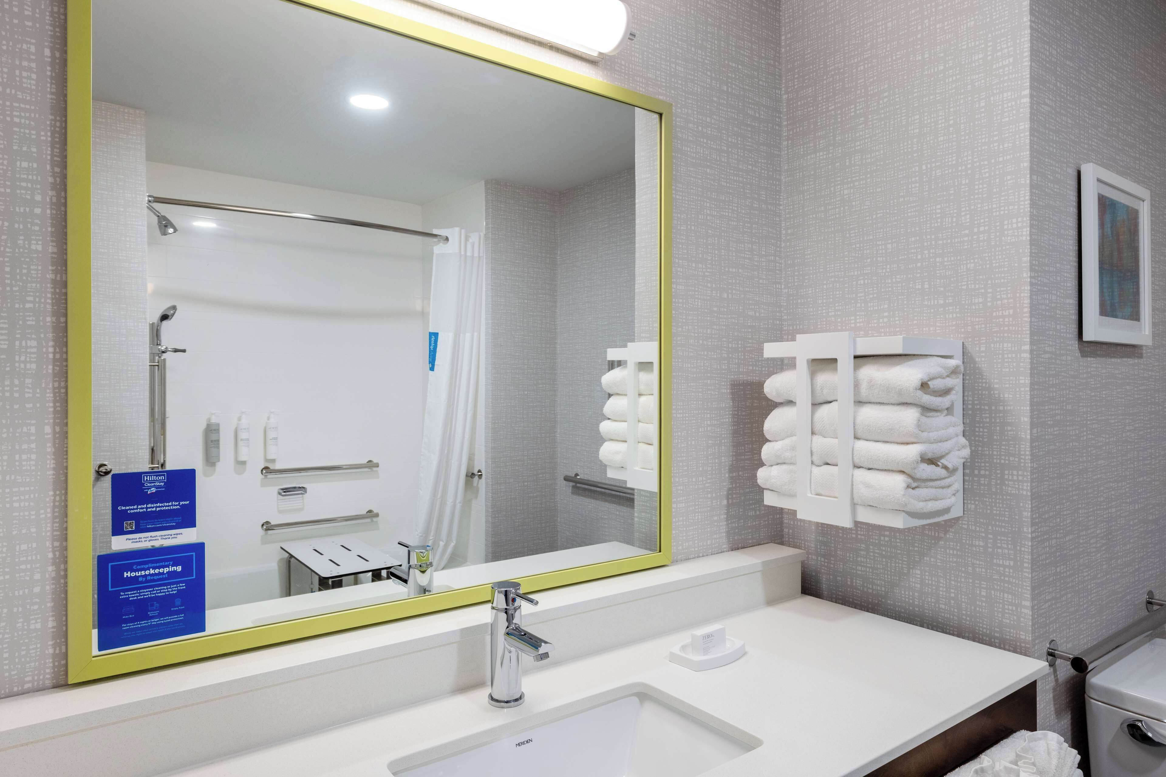 A hotel bathroom with a large mirror, a sink, a towel rack, and a framed picture on the wall.