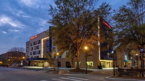 A hotel with a prominent sign, a parking lot, and a street with trees.