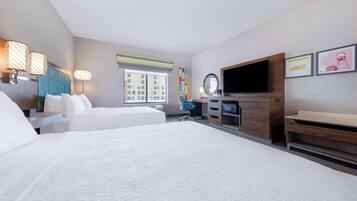 A hotel room with two beds, a desk, a chair, a TV, and a window with a view of buildings.