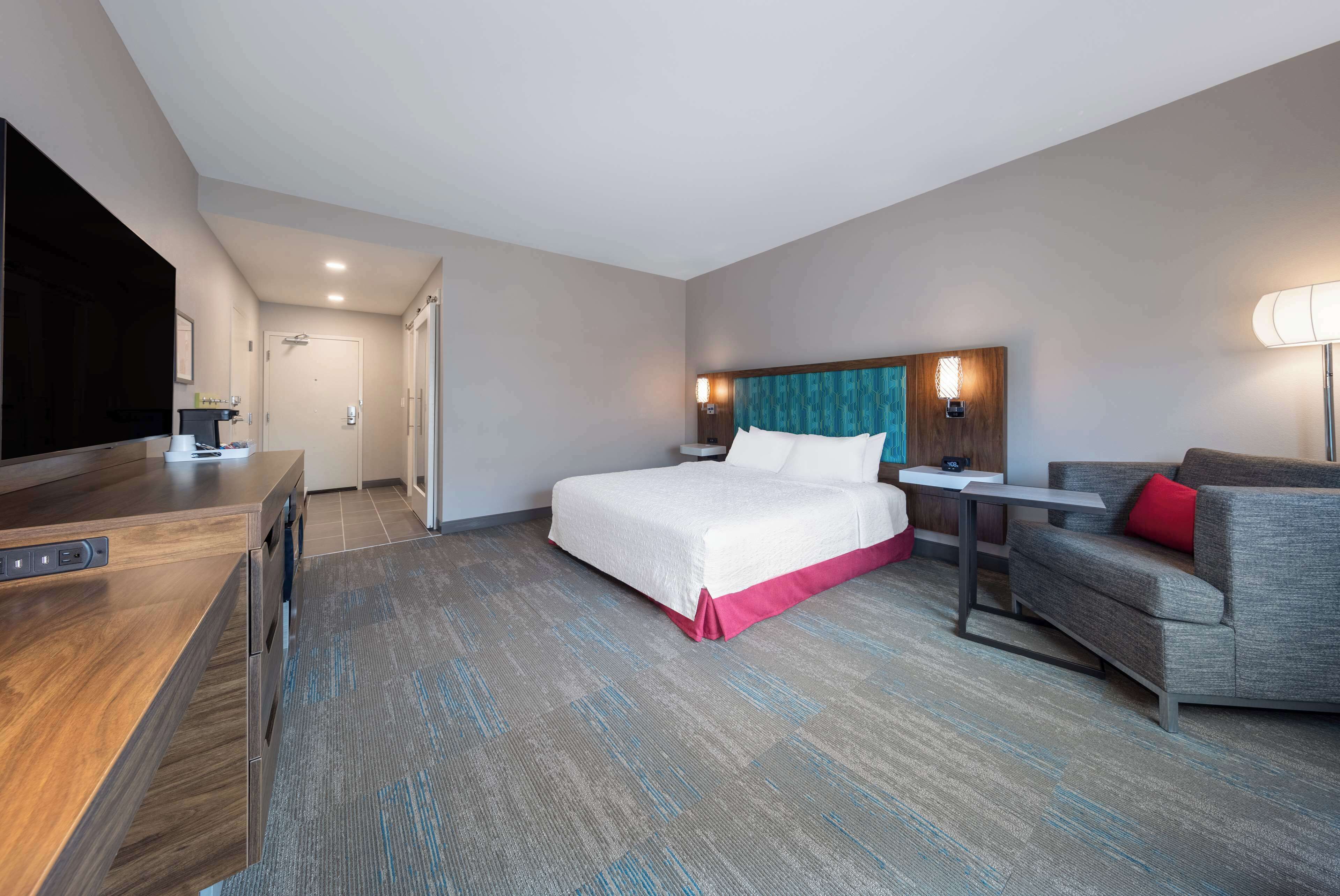 Una habitación de hotel con cama, escritorio, televisor, sofá y lámpara.
