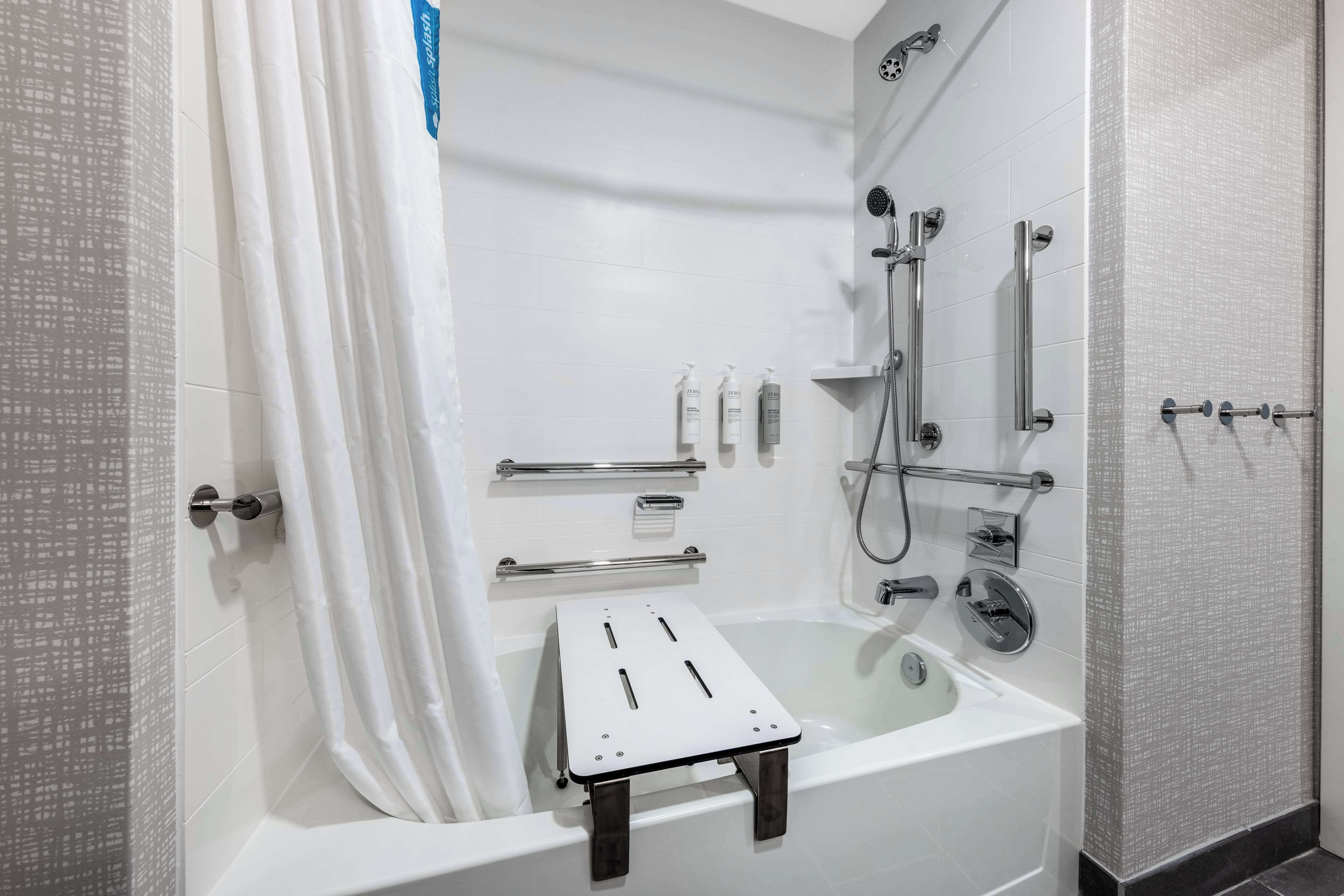 A modern bathroom with a bathtub, shower, and handrails.