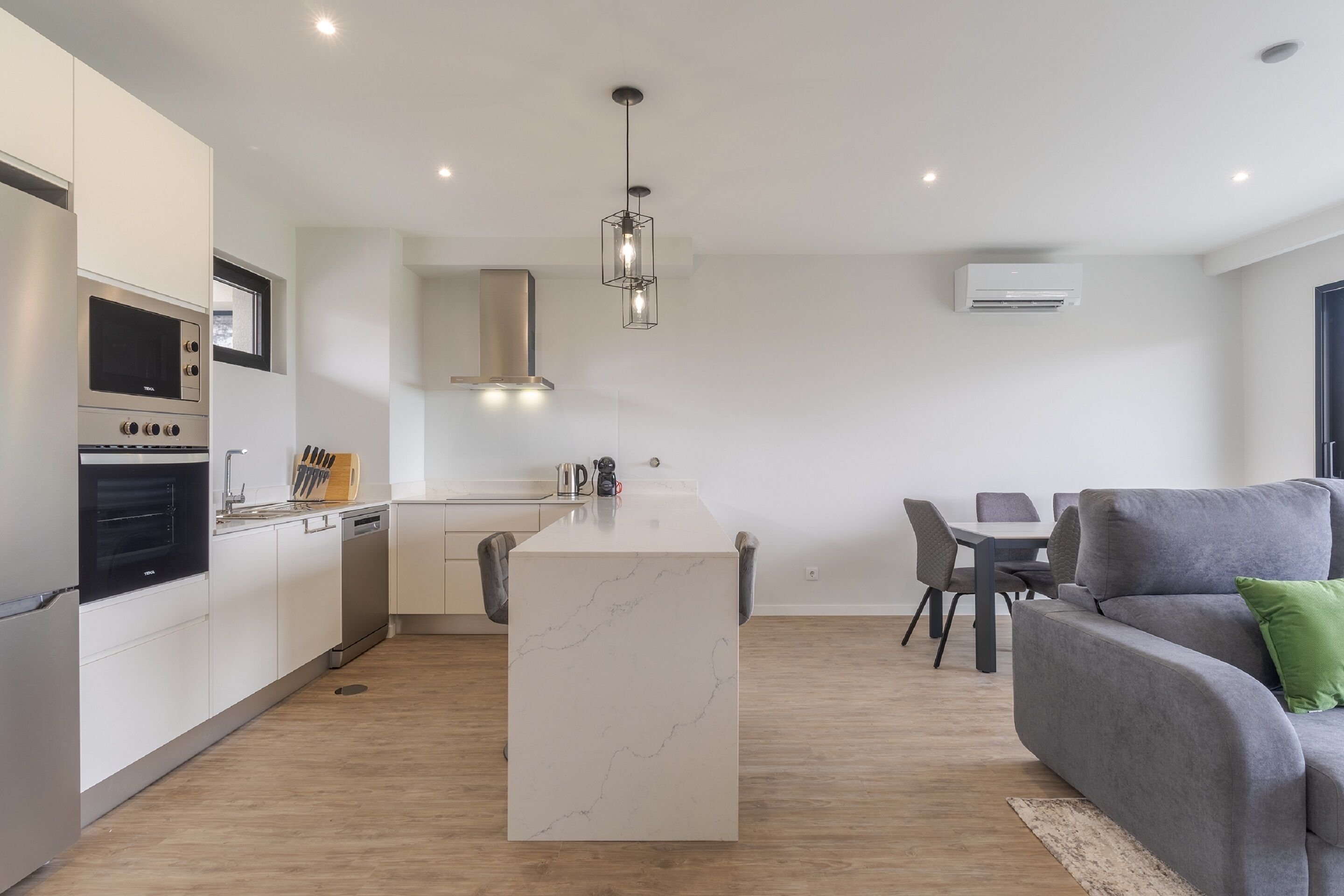 A modern kitchen with built-in appliances, a central island, and a dining area with a grey sofa and chairs.