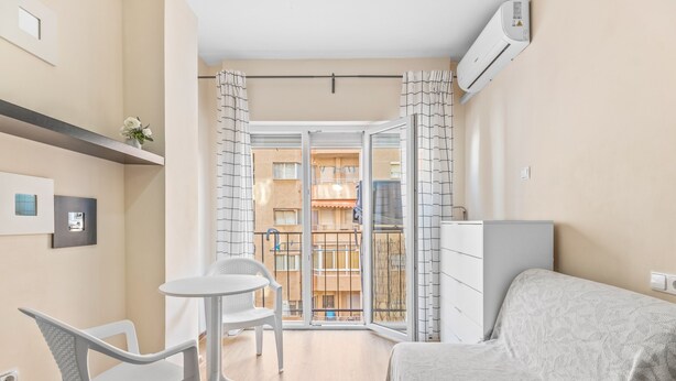 A bedroom with a bed, a small table, a chair, a dresser, and a balcony with a view of other buildings. - Holiday Apartment 200 m from the Beach (Torrevieja)