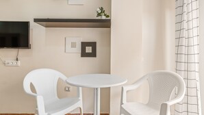 A room with a round table and two white chairs, a TV mounted on the wall, and a small shelf with a plant. - Holiday Apartment 200 m from the Beach (Torrevieja)