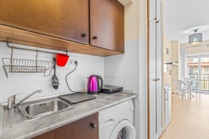 A kitchen with a washing machine, a sink, and a countertop with a kettle and utensils.